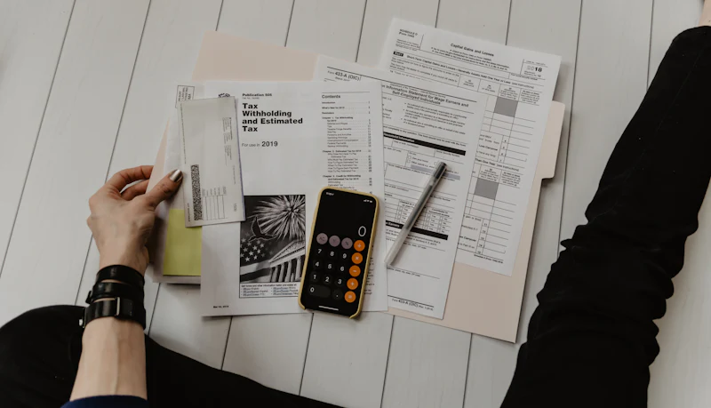 Tax forms, a calculator and a pen laid out on a table