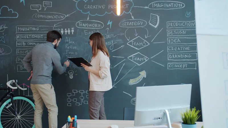 Two colleagues mapping out ideas on a large chalkboard wall