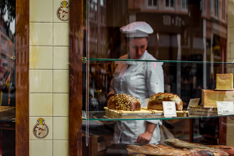A baker in whites arranging seeded loaves in the bakery window