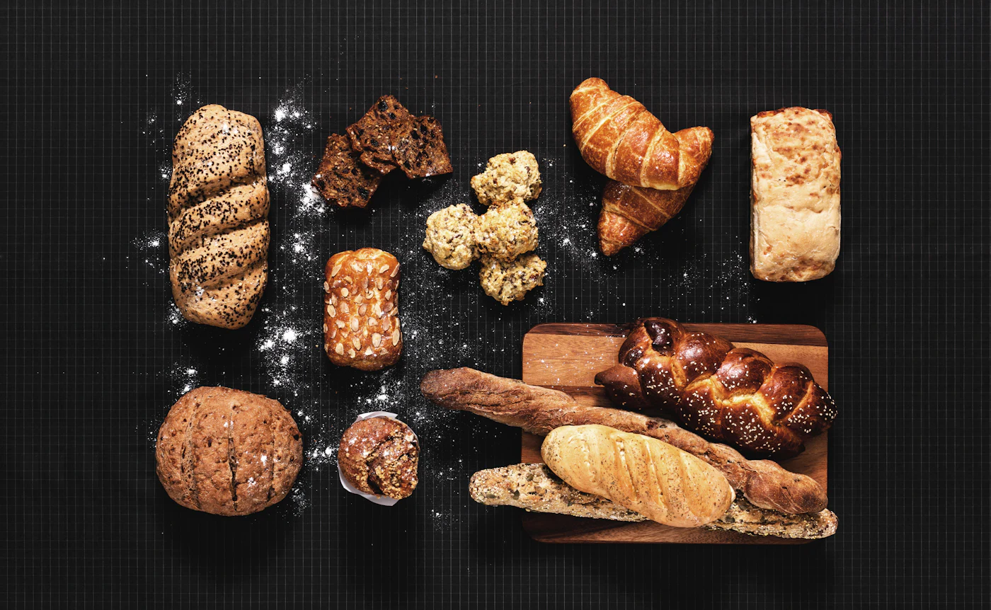 Loaves, croissants and a plaited brioche laid out on a dark table dusted with flour