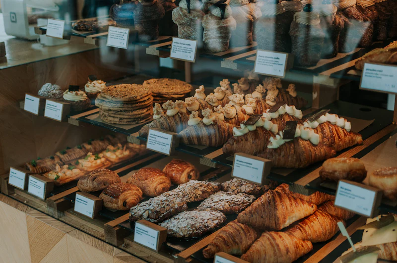 A glass counter filled with croissants, cream-topped pastries and cookies, each with a handwritten label