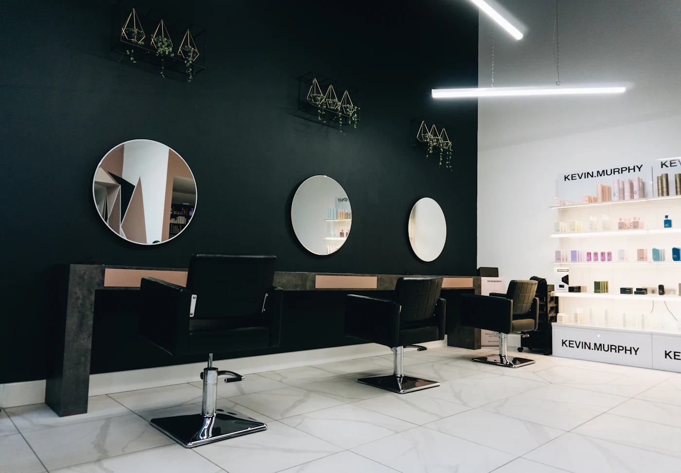 Inside the salon: three styling chairs facing round mirrors on a dark wall, with product shelves to the right