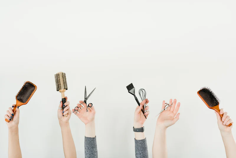 Hands holding up brushes, scissors and a colour brush against a white wall