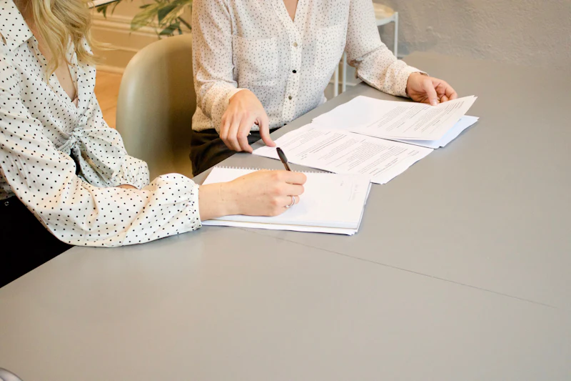 Two people at a meeting table reviewing and signing documents